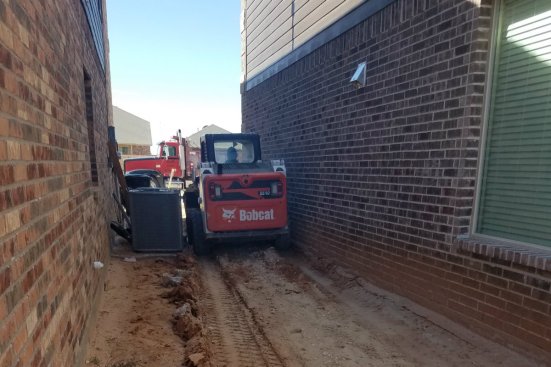 With only inches of clearance, the Bobcat makes its way past the HVAC unit.