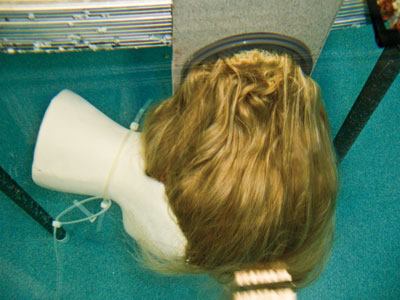 A manufacturer’s

product-development test pictured above, is similar in principle to

the drain-cover standard’s protocol. (Photographed from the

top of the tank. Fitting is installed on the wall.) Testing for

certification is more strict — outlet fittings must be

installed on a larger section of wall or floor, and special

equipment is used to suspend the wig and measure the force required

to remove it.